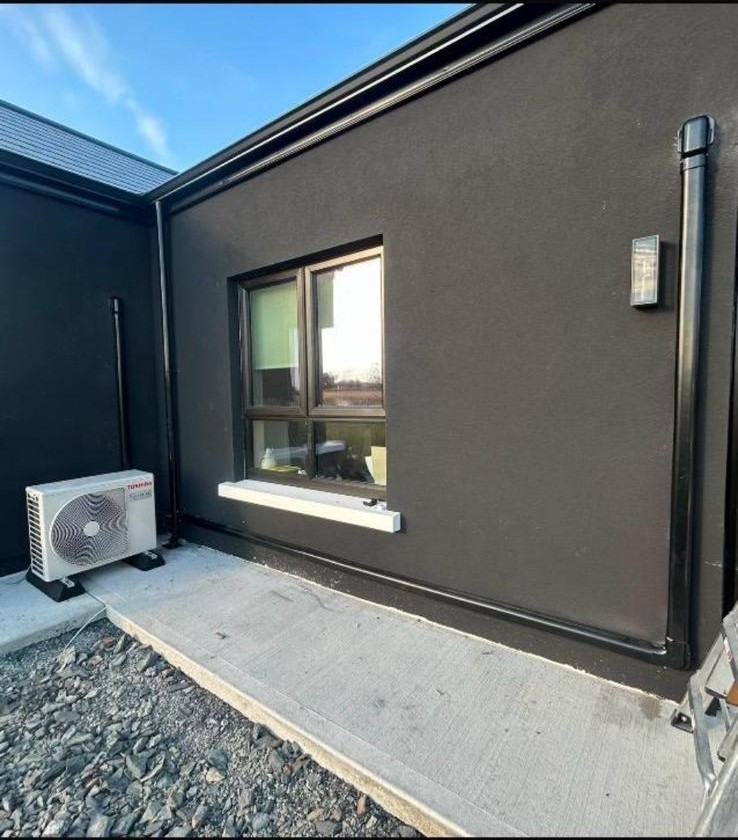 Outdoor air conditioning unit with tidy black pipework on a modern home